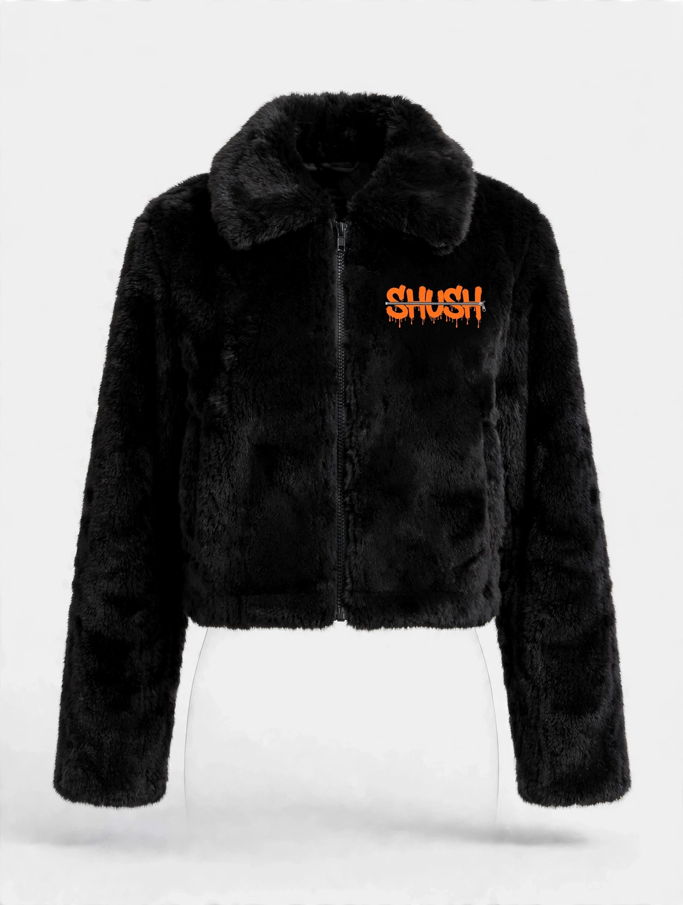 Women's cropped black faux-fur jacket, front view — plush fur, zip front, and a small embroidered SHUSH mark at the left shoulder: the word SHUSH in orange dripping letters zipped shut by a silver zipper
