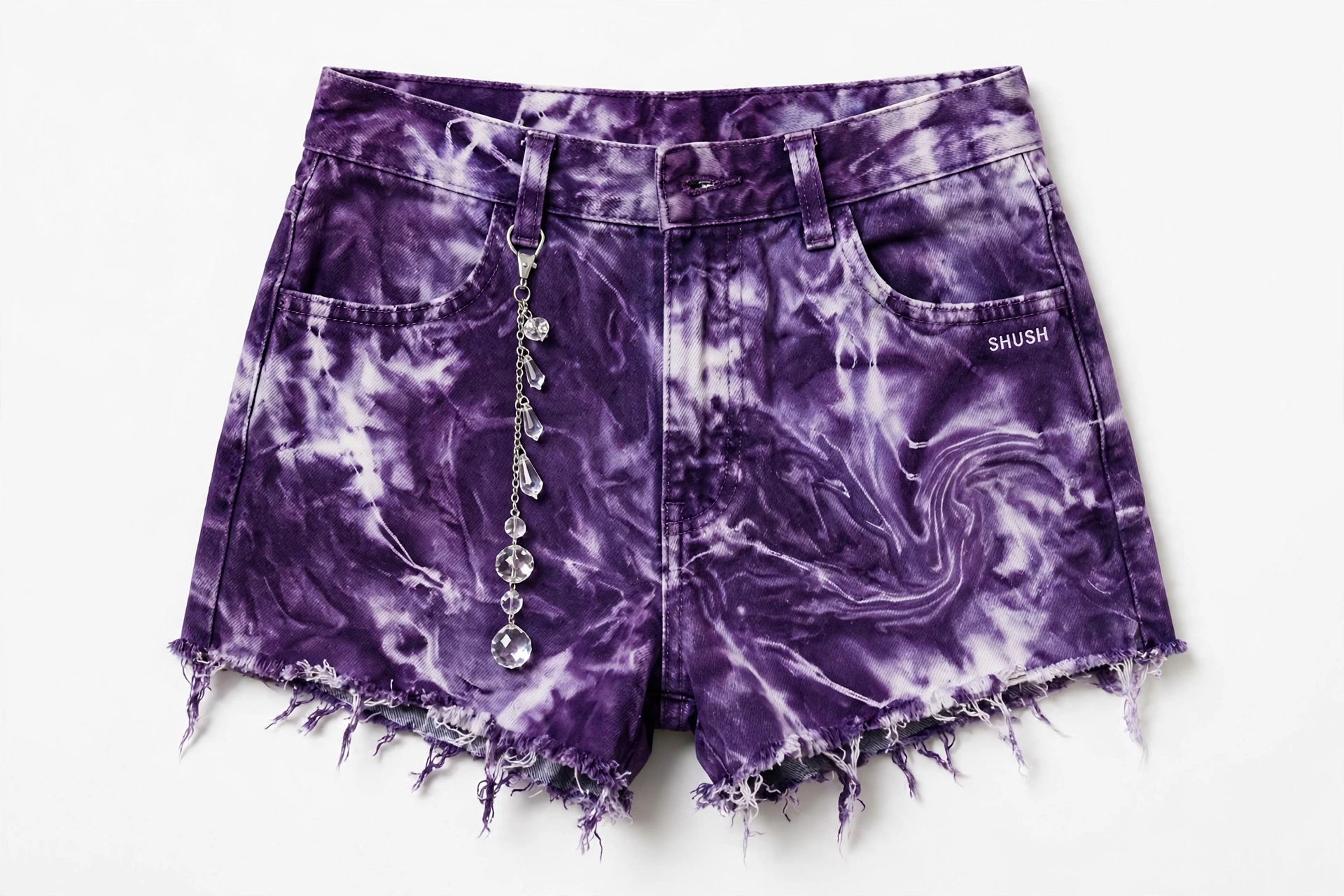 Women\u2019s denim cutoff shorts in a grape-purple marble tie-dye wash with a frayed hem, a small white SHUSH by the front pocket and a silver chain of clear crystal gem drops at the belt loop